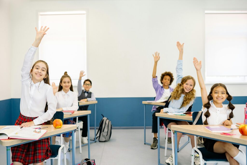Group of diverse children eagerly raising hands in a bright classroom setting.